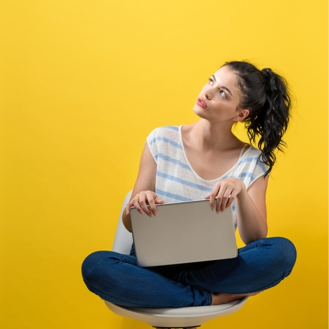 Website Copywriting - When to use 'I' vs 'We' - image of a lady thinking about her website copywriting. She's sitting cross legged with laptop in her lap